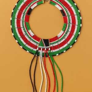Traditional Pokot beaded necklace in red, green, black, and white with cowrie shells, displayed on a warm beige background.